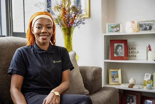 TheKey caregiver relaxing on a sofa in a client's home surrounded by family photos, reflecting a warm and trusting in-home senior care relationship built on comfort and familiarity