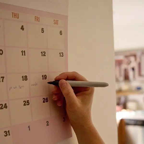 TheKey caregiver writing appointments on a wall calendar, reflecting the organized scheduling and proactive care planning that ensures consistent and reliable senior in-home care service delivery