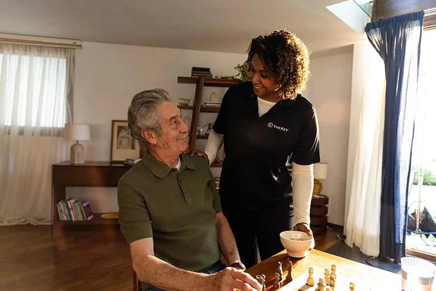 TheKey caregiver engaging with an elderly male client playing chess at home, providing companionship and personalized in-home senior care to support aging-in-place independence