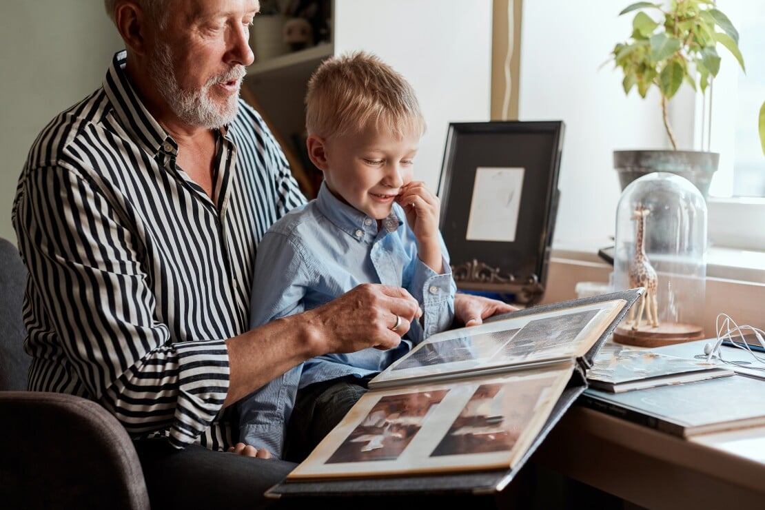 Grandfather and young grandson looking through a family photo album together, illustrating how children can connect with seniors experiencing memory loss and dementia